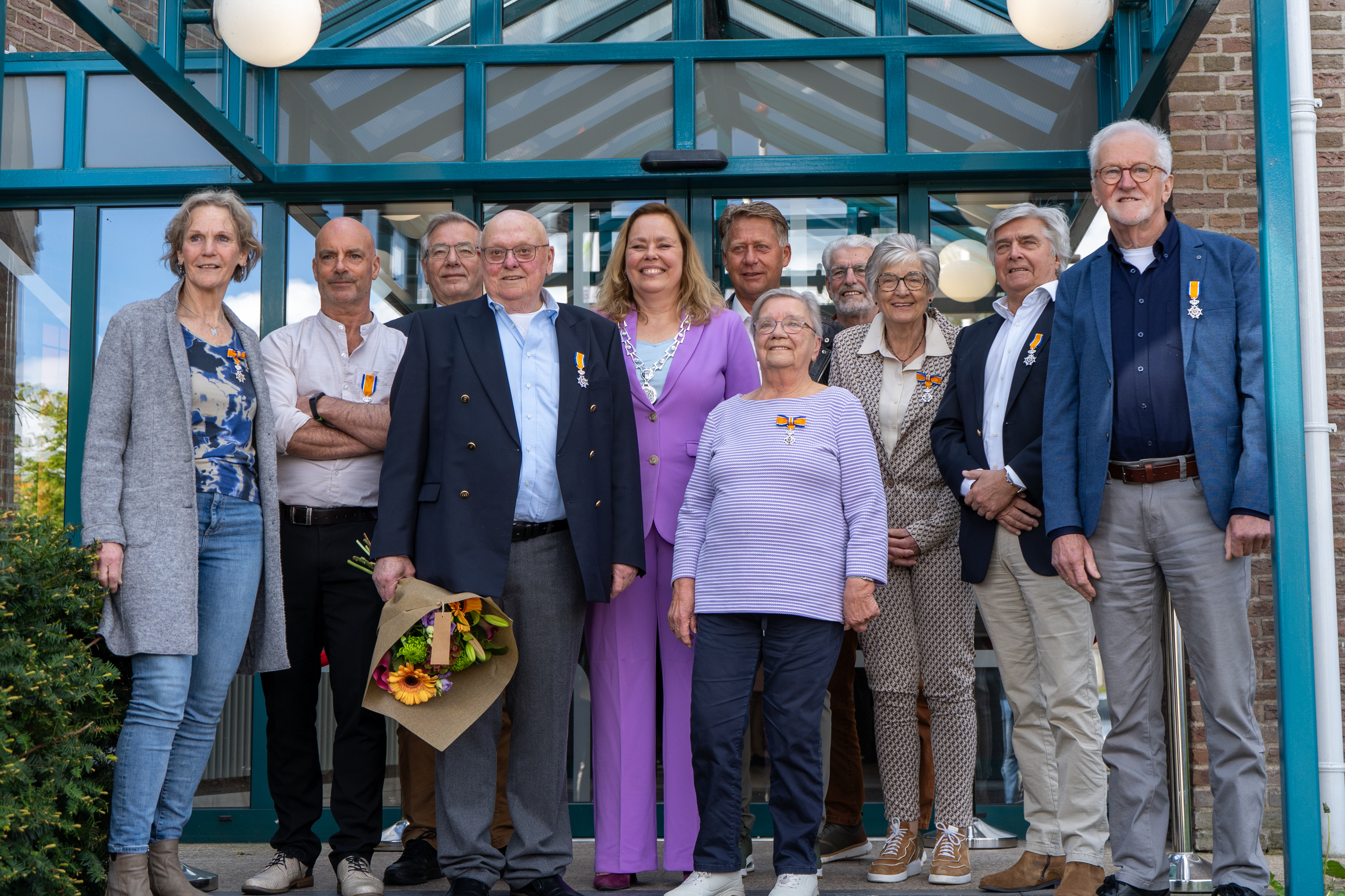 Voor het gemeentehuis staan de gedecoreerden samen met burgemeester Astrid Heijstee van gemeente Kaag en Braassem.