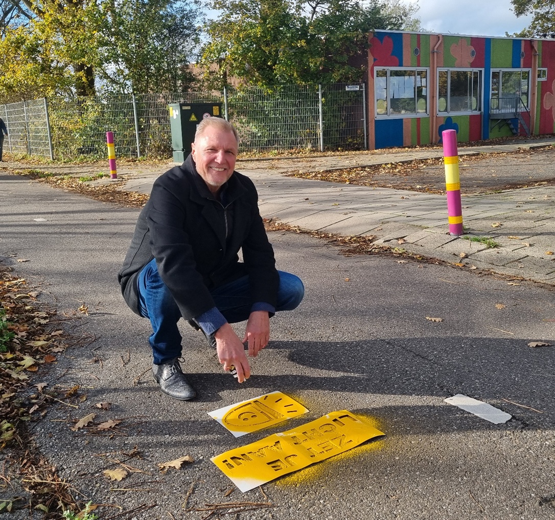 Wethouder Dolf Kistemaker met spuitverf bij een zojuist gespoten tekst 'zet je licht aan'