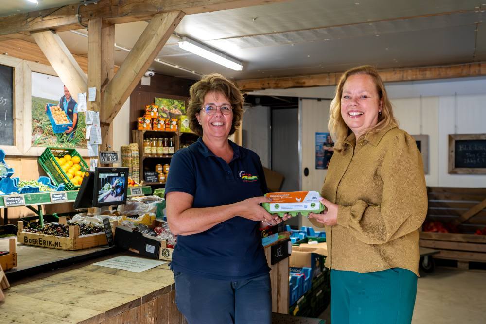Burgemeester Astrid Heijstee met een eierdoos in haar hand, bij boerderij van Rijn