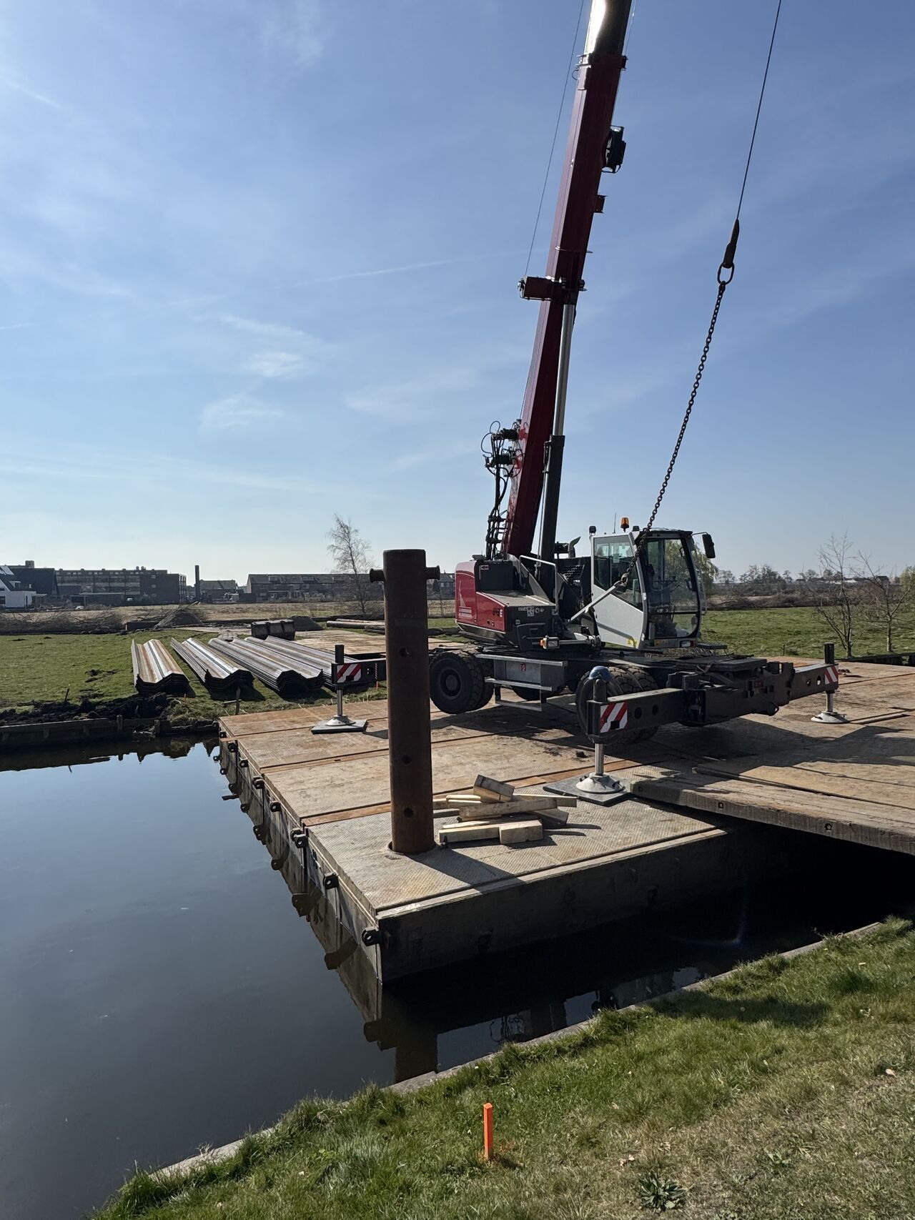 Foto van de werkzaamheden aan de burg. Te zien is een hijskraan op een ponton, beginnende met de werkzaamheden van de brug.